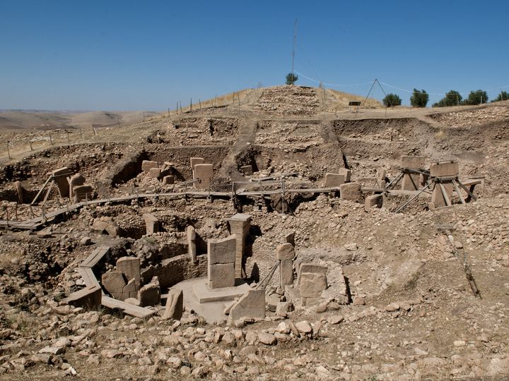 Excavated circular stone enclosures at Göbekli Tepe with tall T-shaped limestone pillars standing among low dry-stone walls on a hilltop