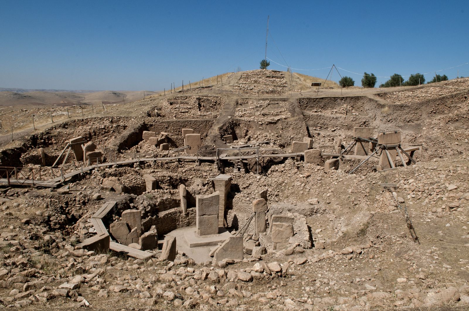 Excavated circular stone enclosures at Göbekli Tepe with tall T-shaped limestone pillars standing among low dry-stone walls on a hilltop