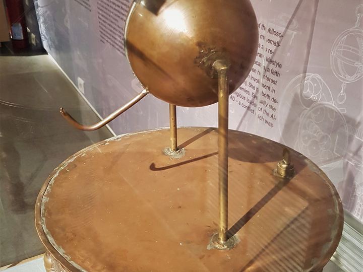 A brass reconstruction of Hero's aeolipile: a metal sphere with two bent nozzles mounted on pipes above a round boiler