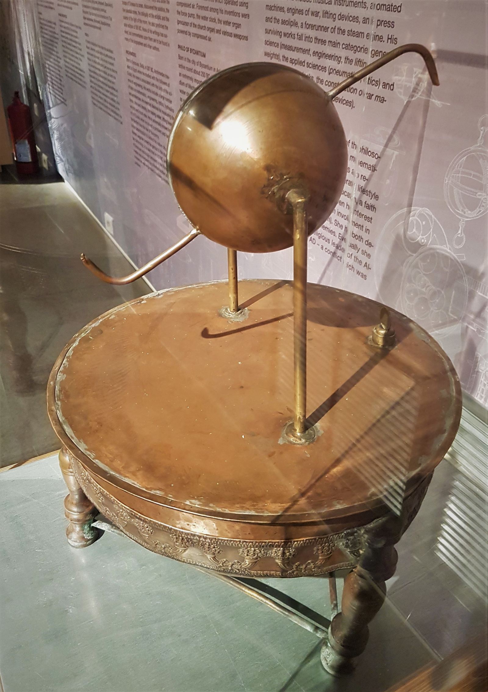 A brass reconstruction of Hero's aeolipile: a metal sphere with two bent nozzles mounted on pipes above a round boiler