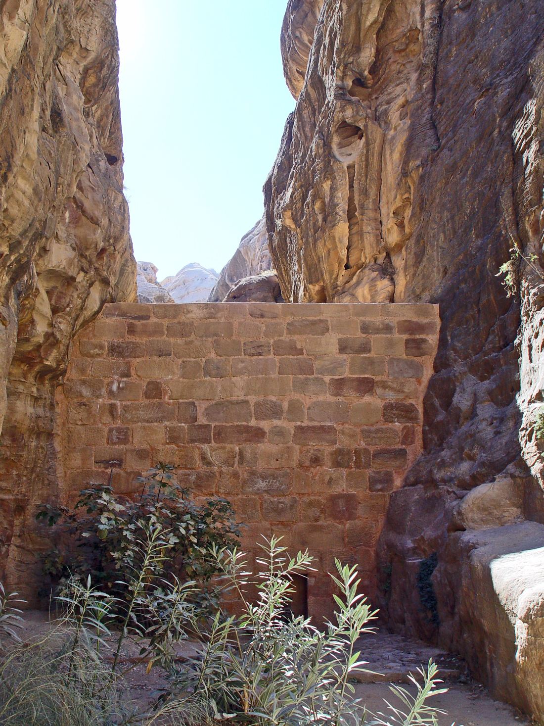 A tall wall of fitted stone blocks closing a narrow gorge between sandstone cliffs at Petra